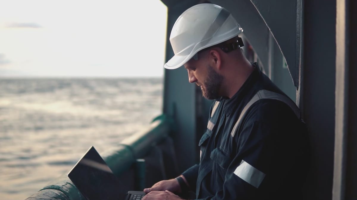 Crew member working on a laptop on deck at sea